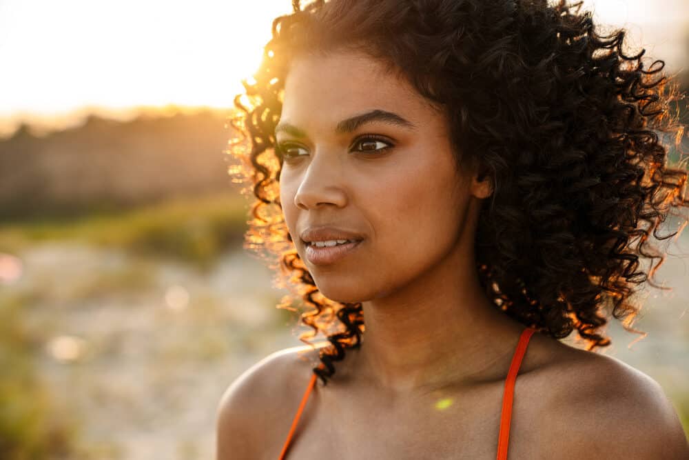 Beautiful African woman with frizz-free bouncy curls walking on the sand at the beach.