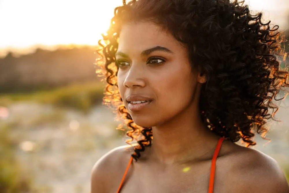 Is Cantu Bad for Your Hair? What About Their Shampoo, Conditioner, and Other Products? 6 Beautiful African woman with frizz-free bouncy curls walking on the sand at the beach.