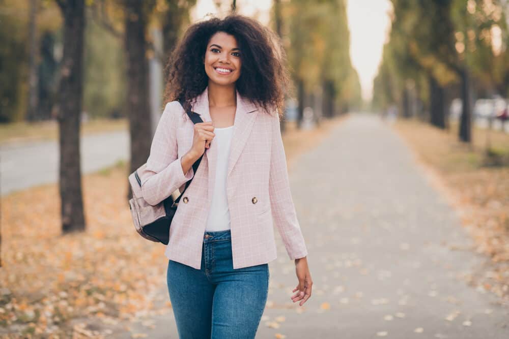 Beautiful woman with dark skin smiles for the camera while walking through a park during fall.