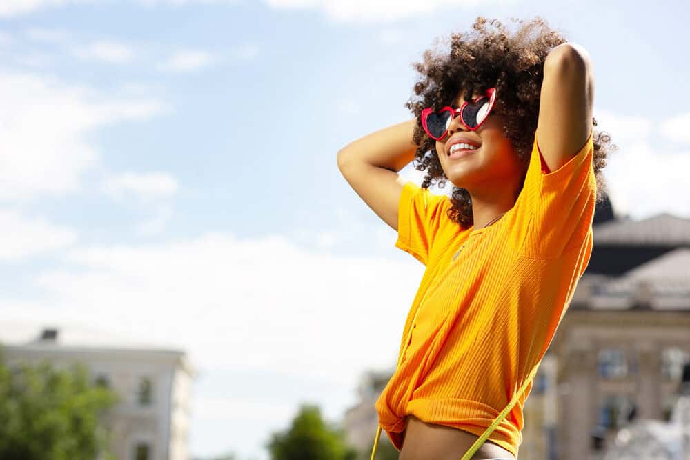 Delightful young woman wearing an orange shirt, blue jeans, and a yellow purse.