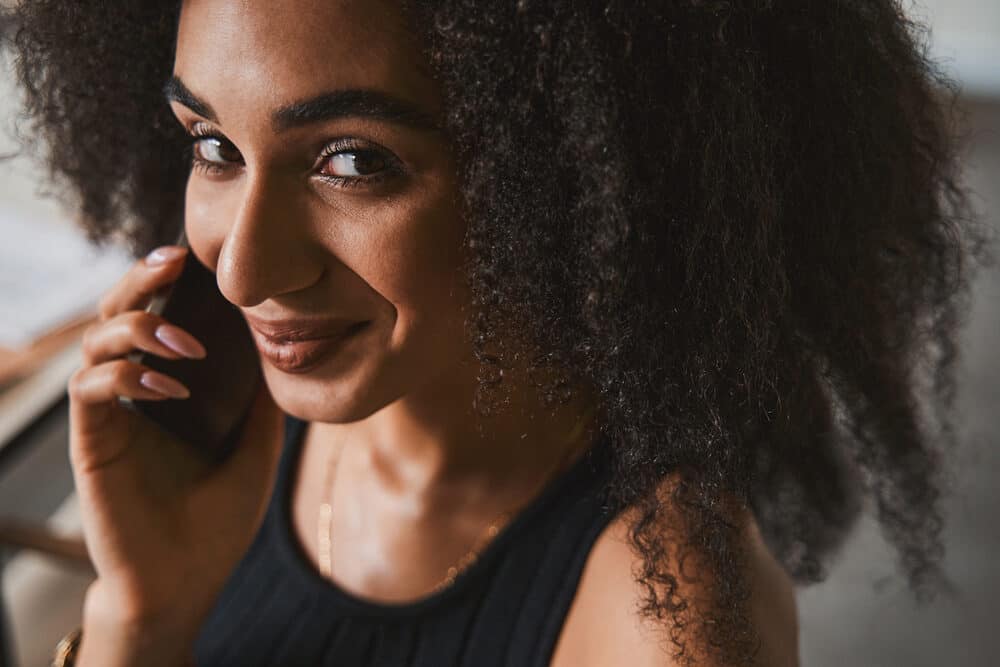 Beautiful curly young woman with color-treated dark hair talking on an Android phone