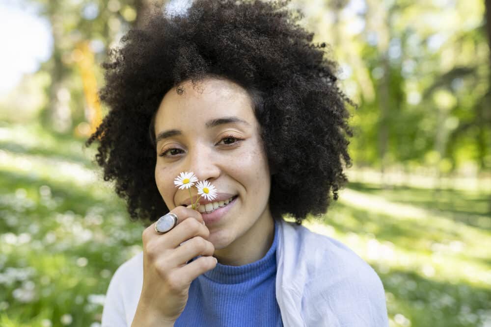 Mixed black girl with smooth skin and coarse hair smelling daisies outdoors