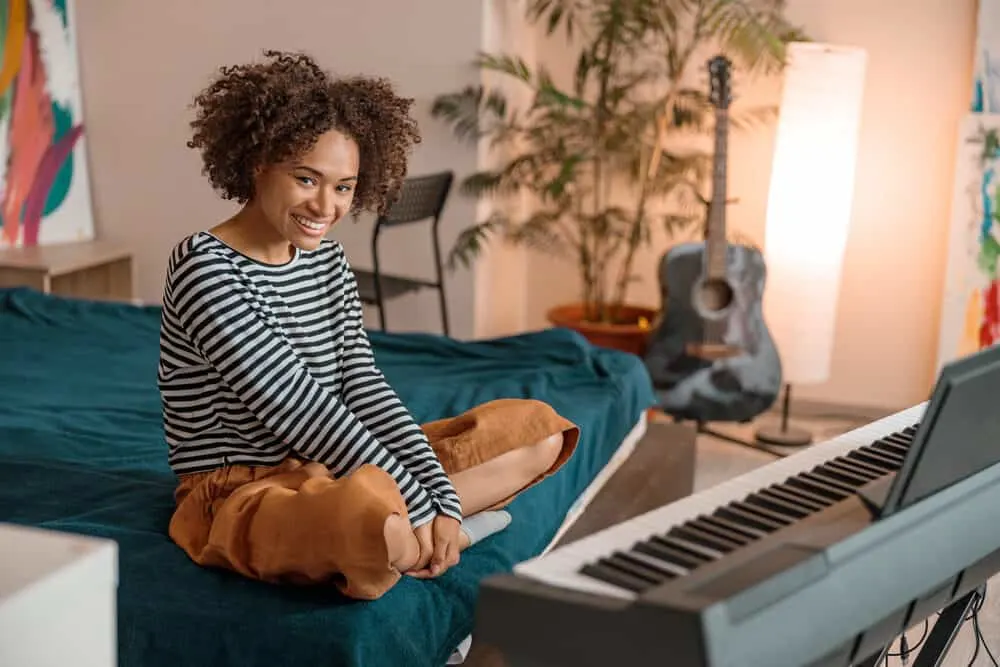 A cheerful black woman with recently dyed delicate hair strands sitting on a bed with musical instruments.