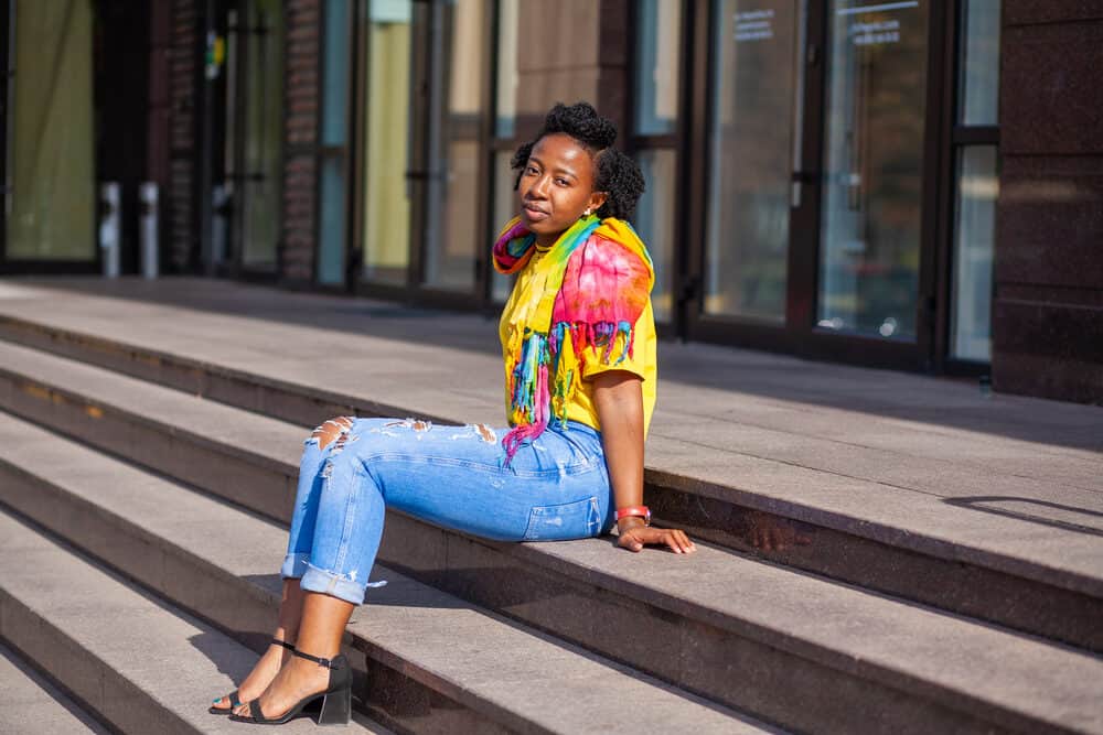 African American female with good scalp health wearing a tie-dyed shirt and blue jeans.
