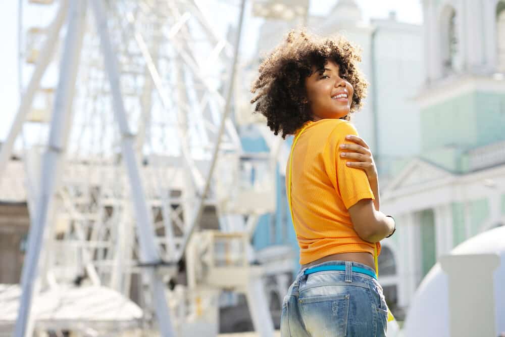 Cheerful black girl wearing an orange t-short and torn jeans at an amusement park.