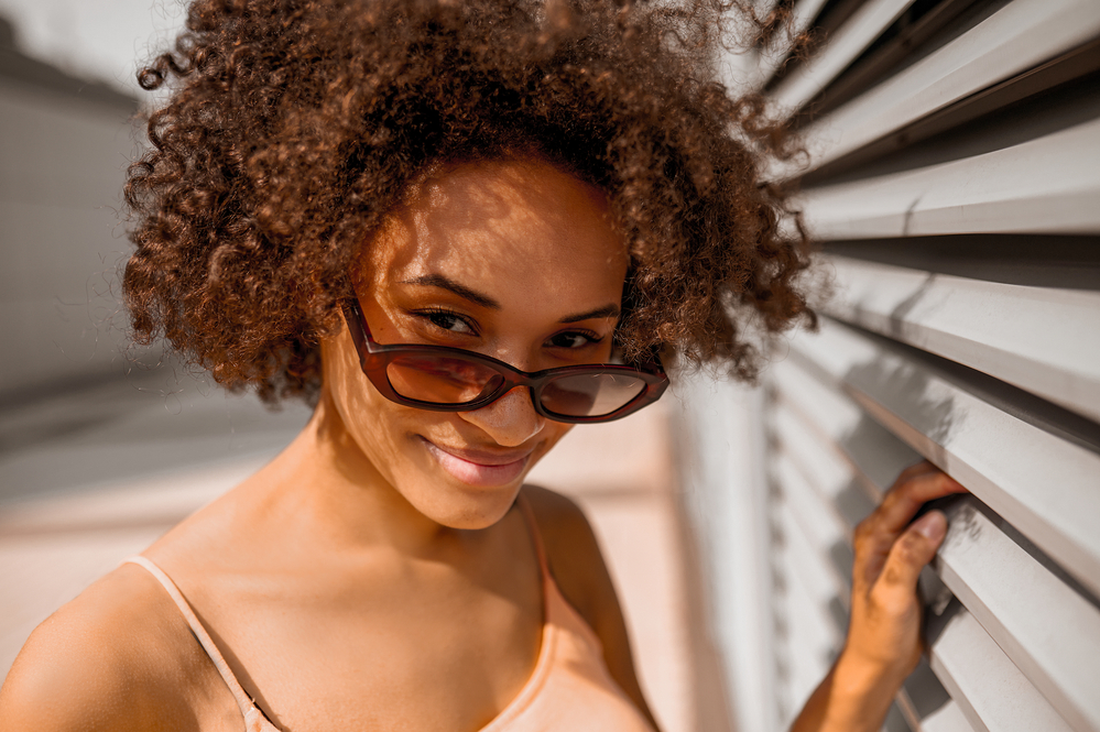 Physically attractive woman wearing sunglasses and spaghetti-strap shirt on a sunny day.