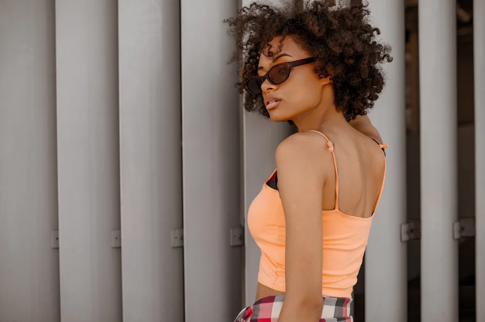 A young cute black girl wearing casual clothes and shades while looking back over her left shoulder.