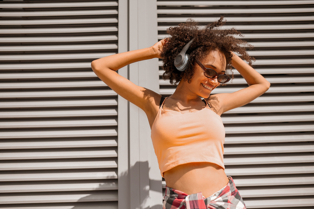 A pretty woman with 4B kinky hair strands listening to music and dancing outside.