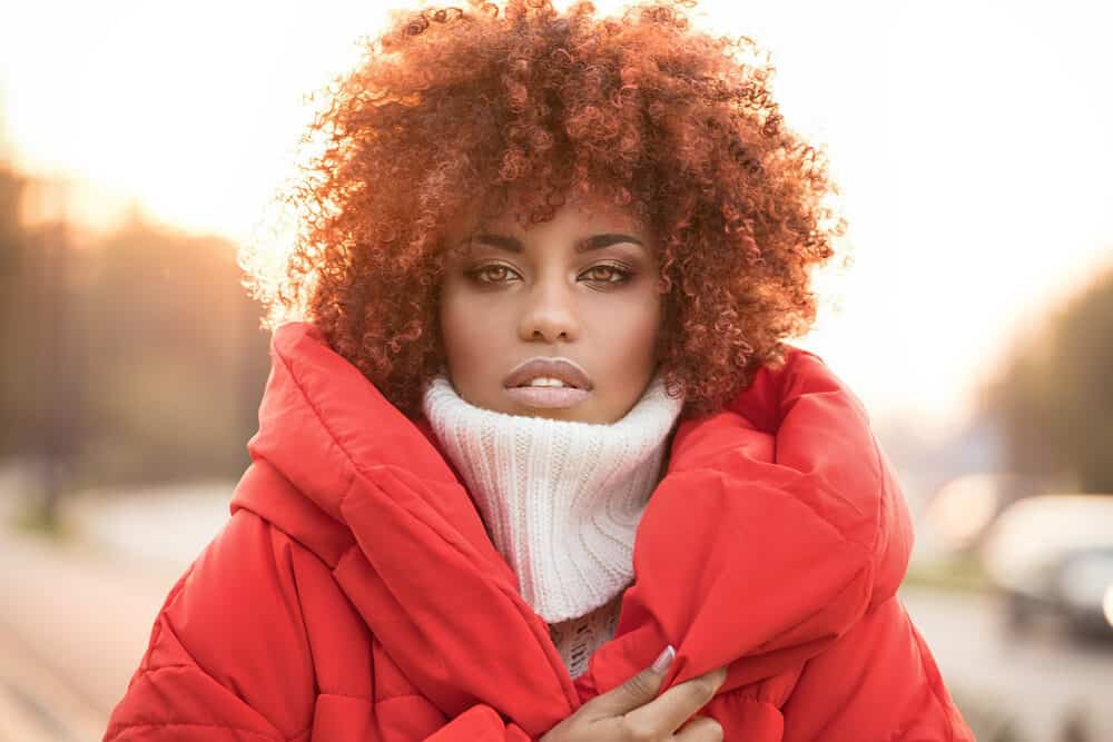 Black women with naturally brown hair wearing a red coat outside on a cold day.