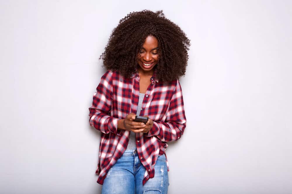 An African woman using a mobile phone to research hair and makeup experts.