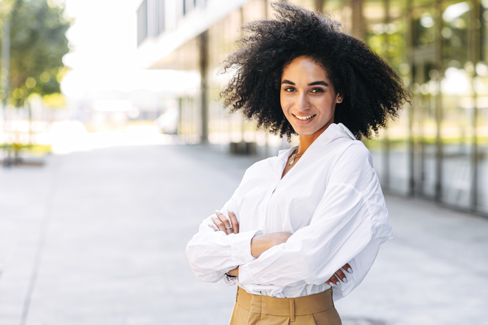 A lady with curly hair follicles standing outdoors in Birmingham, Alabama with her arms folded.