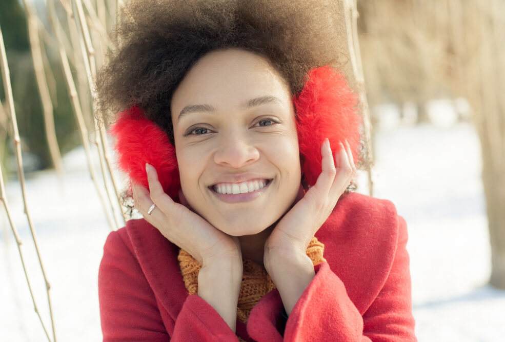 African American woman with kinky knotted hair wearing red earmuffs while chewing gum.