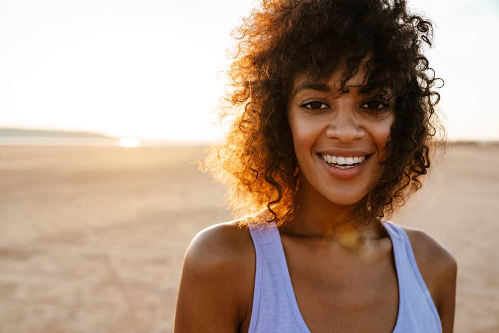 Cheerful African American lady with wavy healthy hair strands with frayed ends walking through the desert.