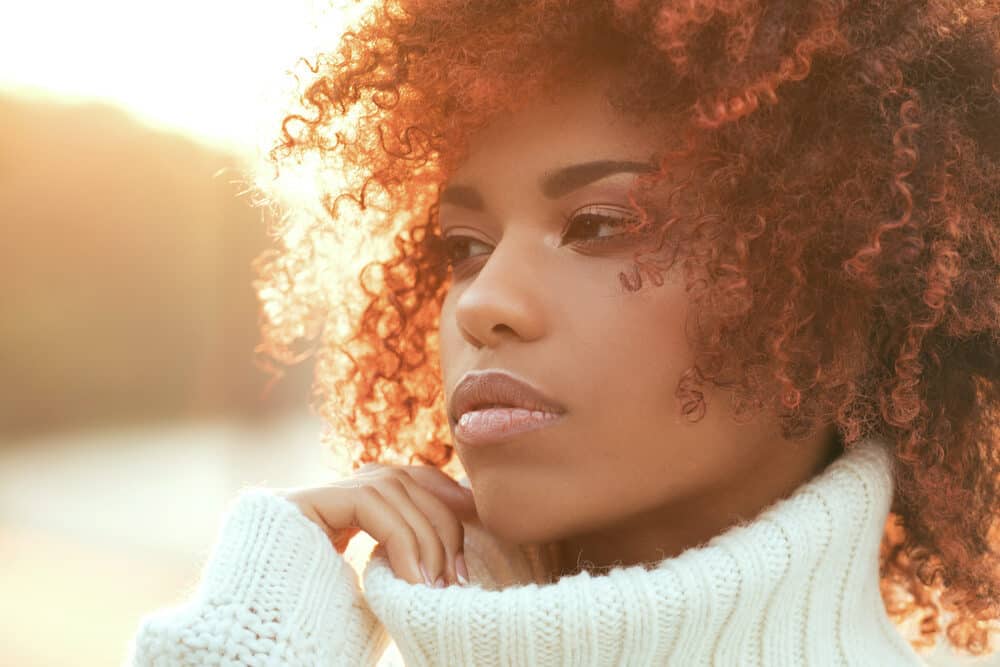 Adult female outside on an autumn day with a chocolate brown curly afro hairdo.