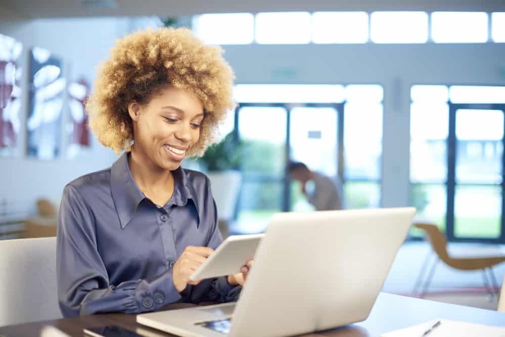 Black lady with caramel skin with new hair growth underneath color-treated hair using a laptop.