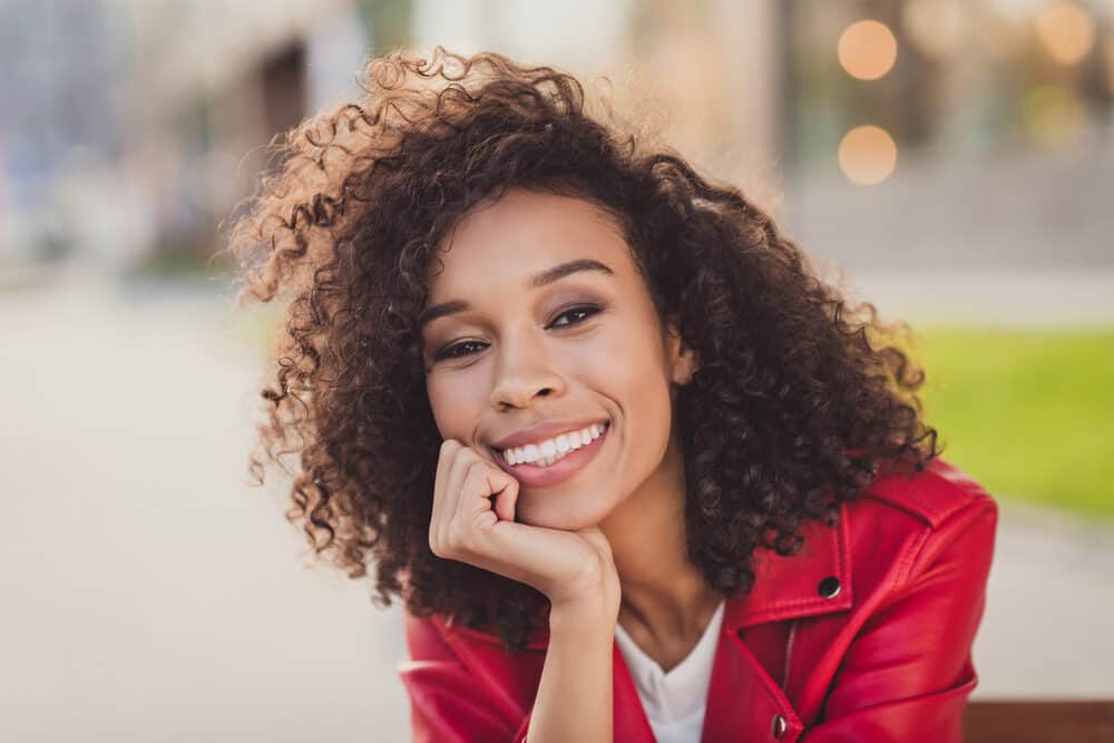 Charming young lady with wavy dry hair dyed brown with semi-permanent hair color wearing a red jacket.