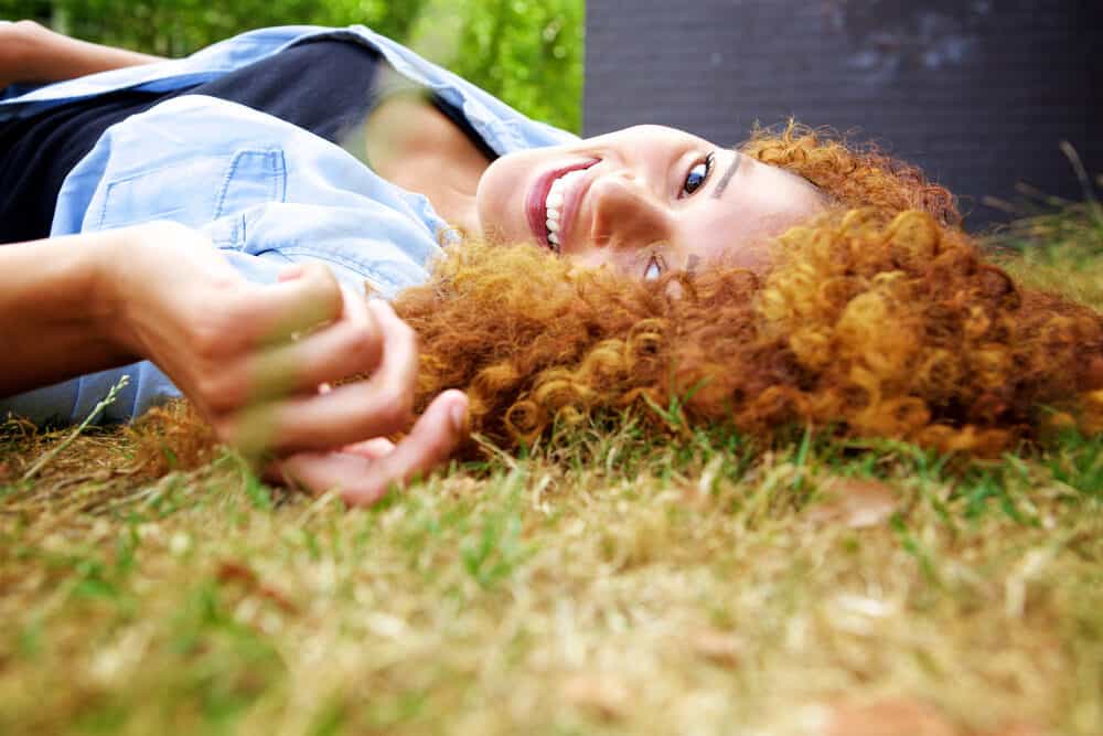 Light skinned black girl with ginger curls styled with a good protein conditioner relaxing outside