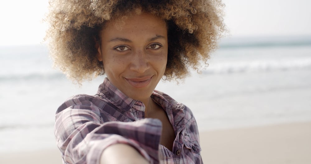 African American woman with a gentle smile wearing blonde bleached hair with dark brown roots.