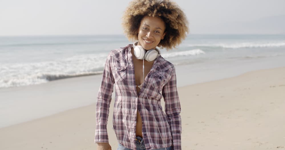 Attractive black lady with yellow blonde curls wearing Beats headphones on the beach.