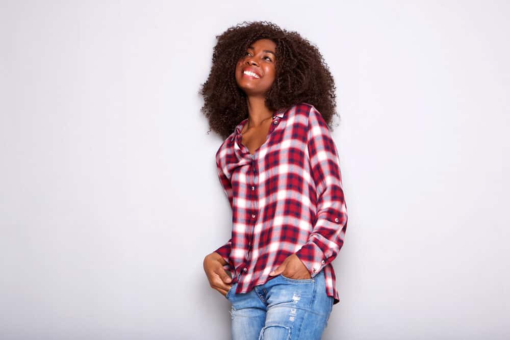 Woman in a checkered blouse planning to get a cosmetology license online smiling and looking to the side.