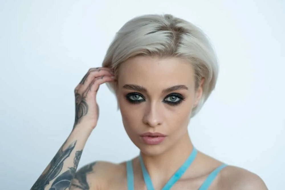 T10 Wella Toner Before and After on Orange, Yellow Hair, and More 9 White lady with tattoos wearing a pale blonde bob with unwanted warmth coming out at the roots