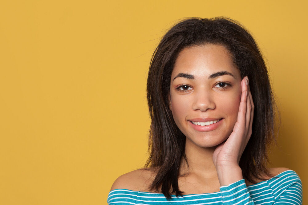 A young woman with thin hair holding the side of her face while wearing natural make-up.