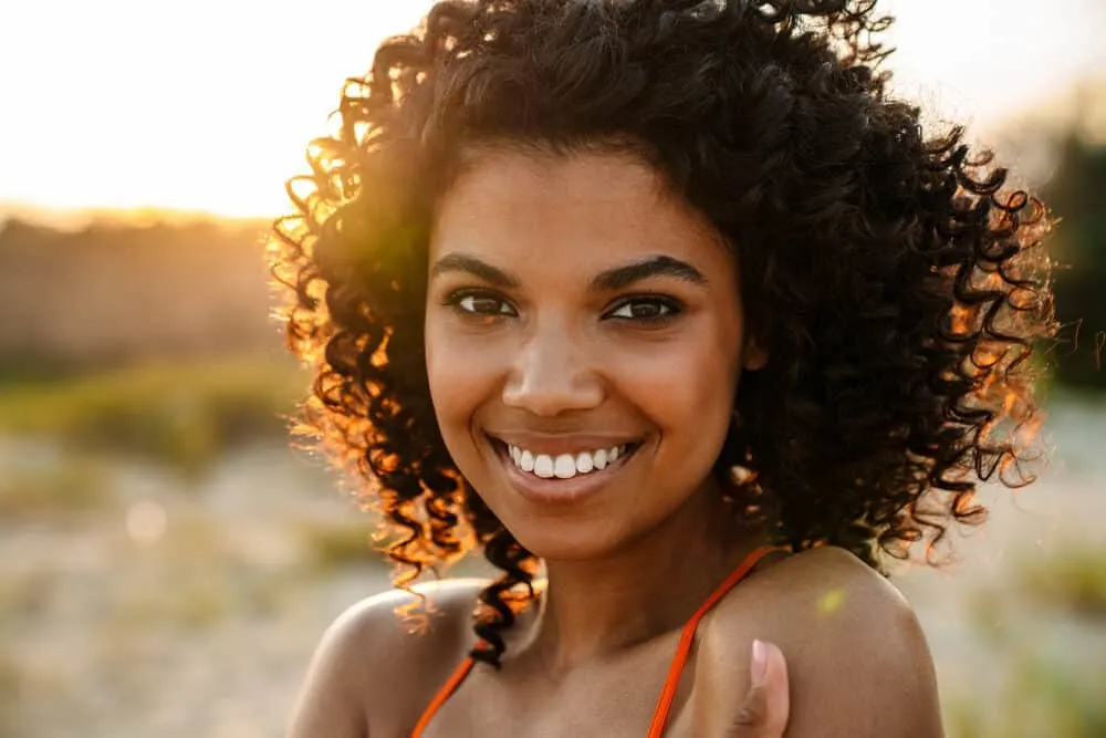 Is Cantu Bad for Your Hair? What About Their Shampoo, Conditioner, and Other Products? 1 Young African American woman with a curly hair type styled with Cantu shea butter and Cantu curl activator cream.