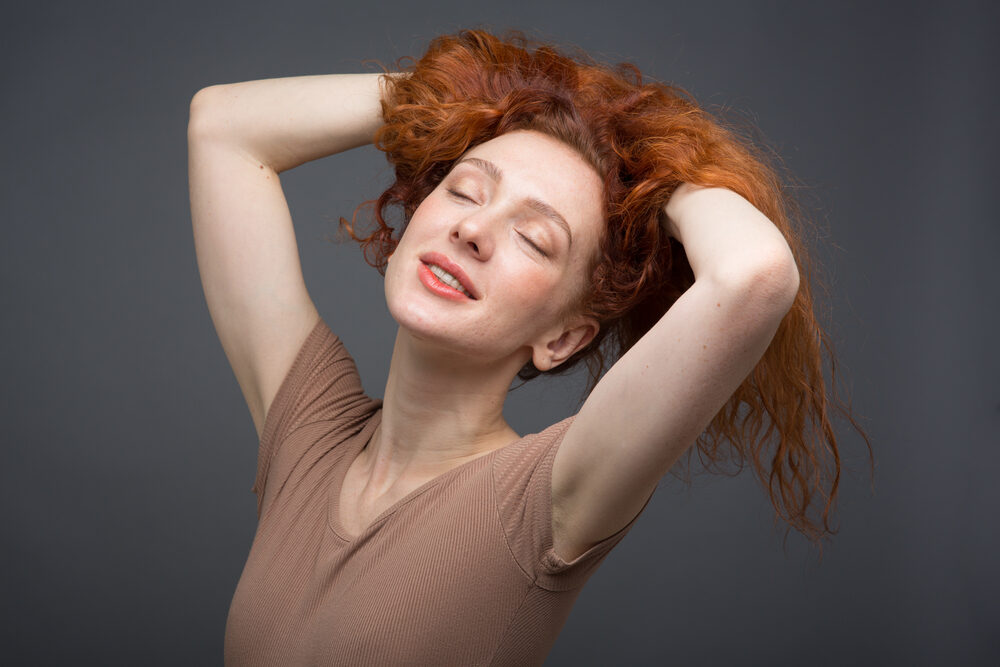 Cute white woman playing in her hair that has orange tones and reddish-brown natural color.