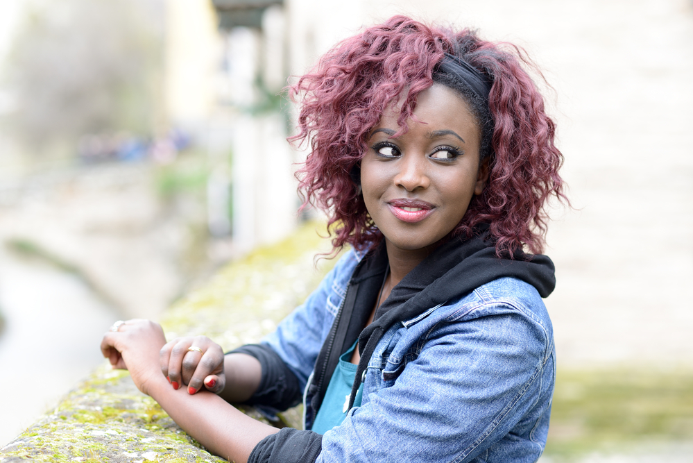 Woman with dyed black hair wearing a blue jean jacket and red fingernail polish.