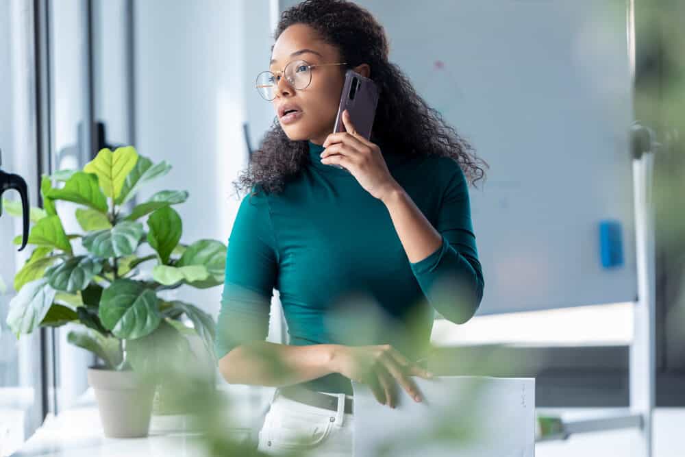 A business woman with curly permed hair on a dark hair color talking on the phone at her workplace.