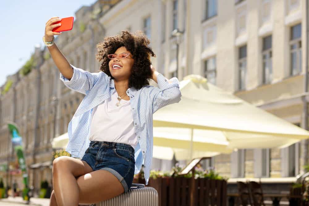 Cute black girl wearing casual clothes talking a selfie of her changes in hair color in the sunlight.