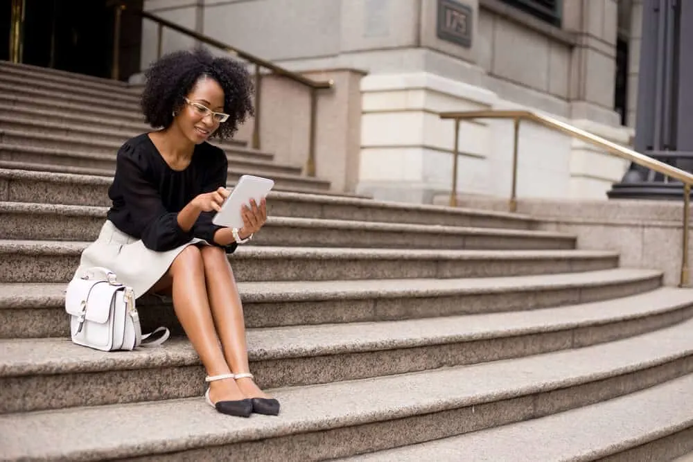 Hair Breakage on Top of Your Head: Causes, Fixes, Products, and More 6 Attractive young African American female using a tablet with curly new growth around her edges.