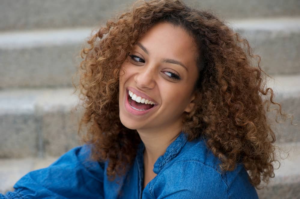 Happy young black woman sitting outdoors with shadow root hair strands with a seamless blend.