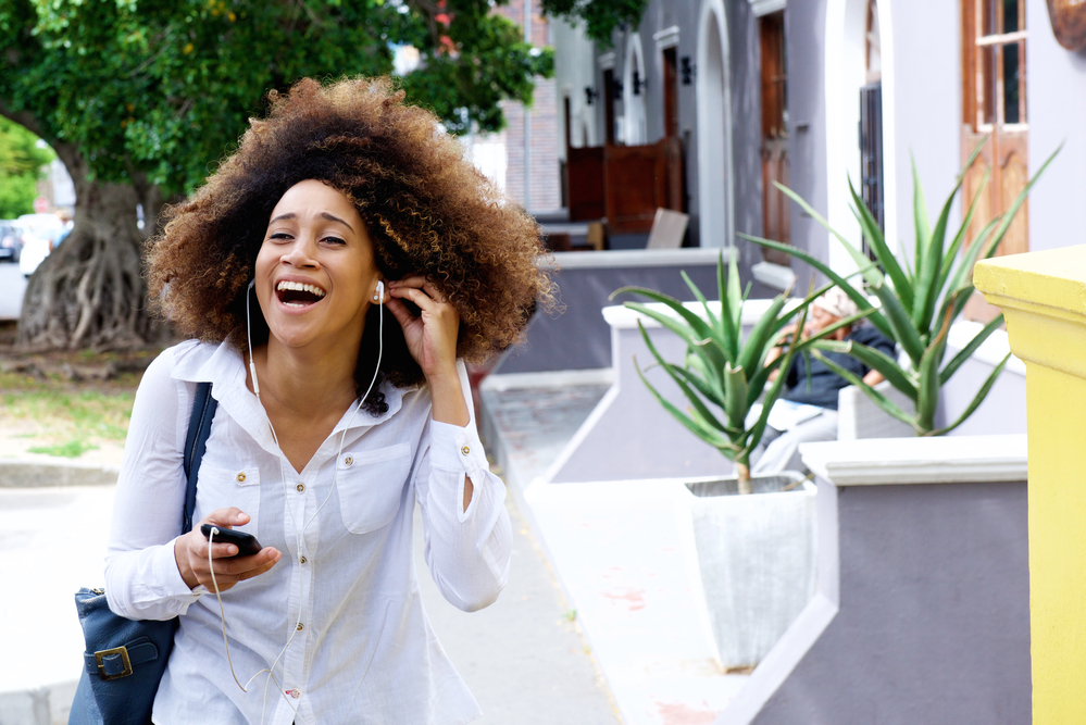 Young black woman with ultra-rich super thick hair on the phone laughing.