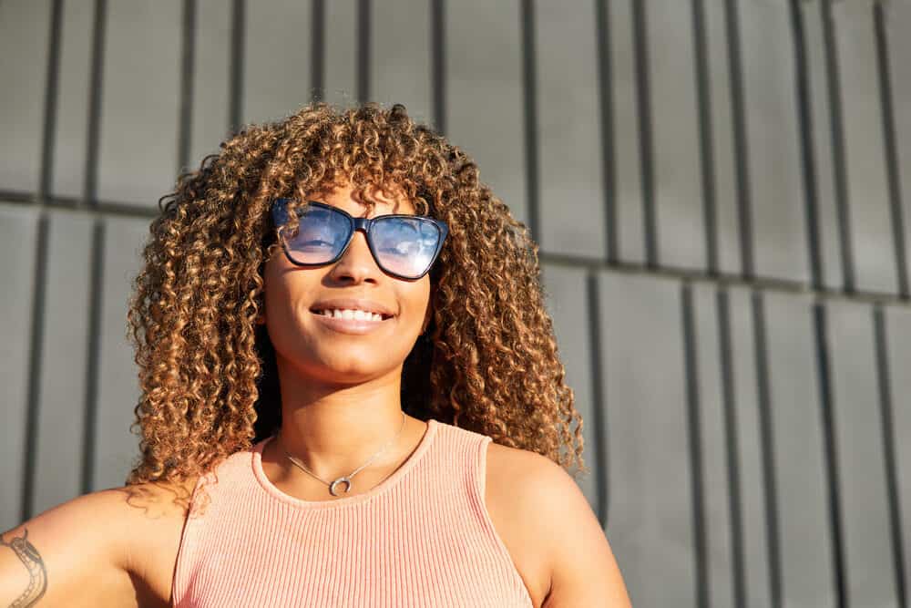 Adult female with reddish hair dye on bouncy 4A natural curls after lightening hair with bleach and lemon juice.