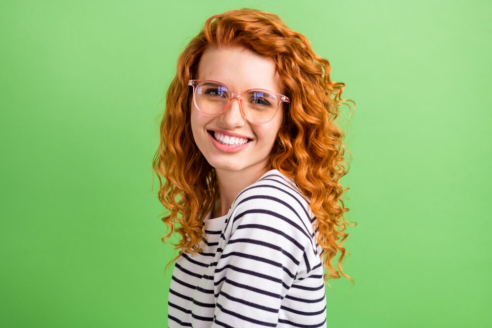 Adorable young woman with wavy bright copper auburn hair wearing a black and white shirt.