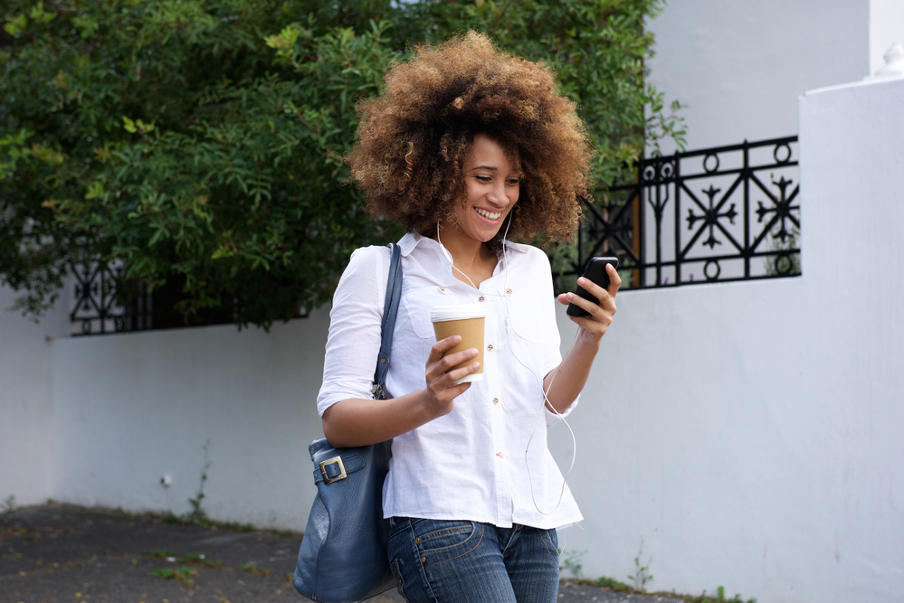 Cute woman with pre-bleached natural hair walking down the street drinking coffee. 