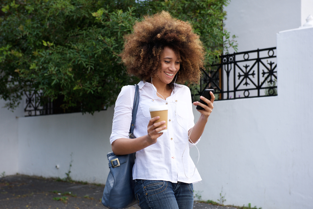 Cute woman with pre-bleached natural hair walking down the street drinking coffee.