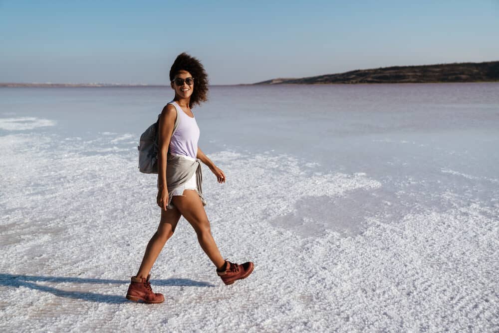 Cute black girl wearing a purple shirt and white shorts shoulder length or longer hair walking in the sand.