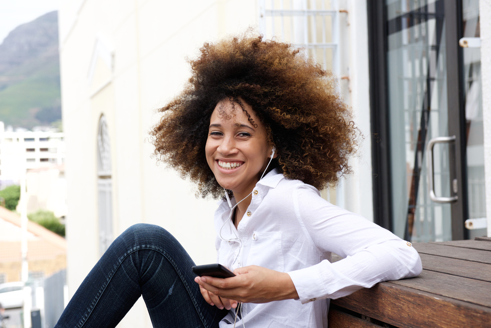 African American female with a dark brown natural hair color sitting outside with talking on the phone.