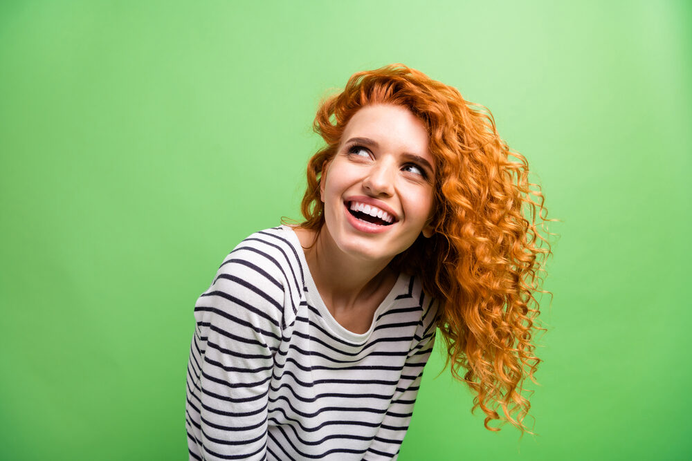 Charming young female with red-orange human hair smiling while looking into the distance.