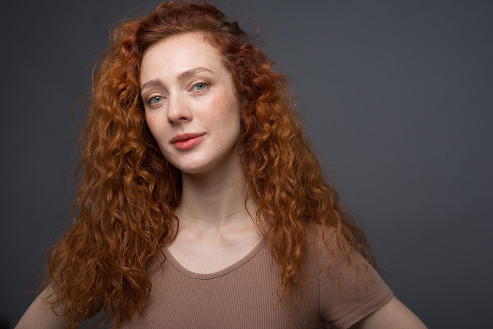 Caucasian female leaving her hair stylist with wavy red hair strands.