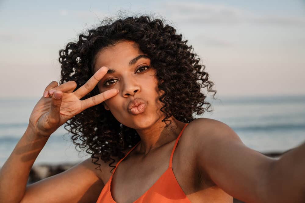 Positive black girl at the beach wearing 4A defined curls styled without harsh chemicals keeping her hair moist.