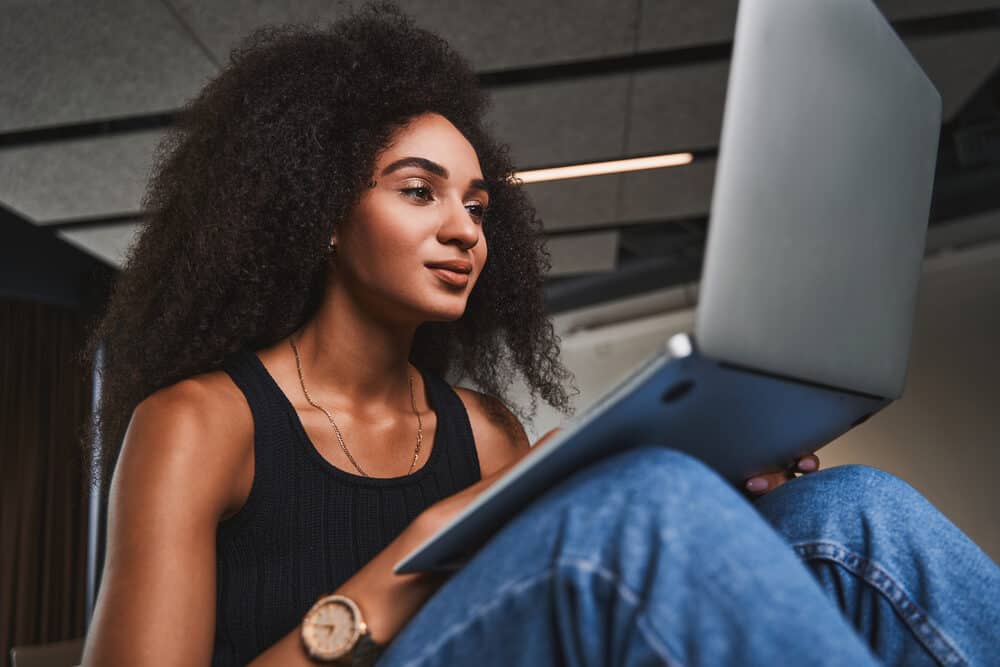 Beautiful young woman with color-treated hair with brassy tones using a laptop wearing casual clothes