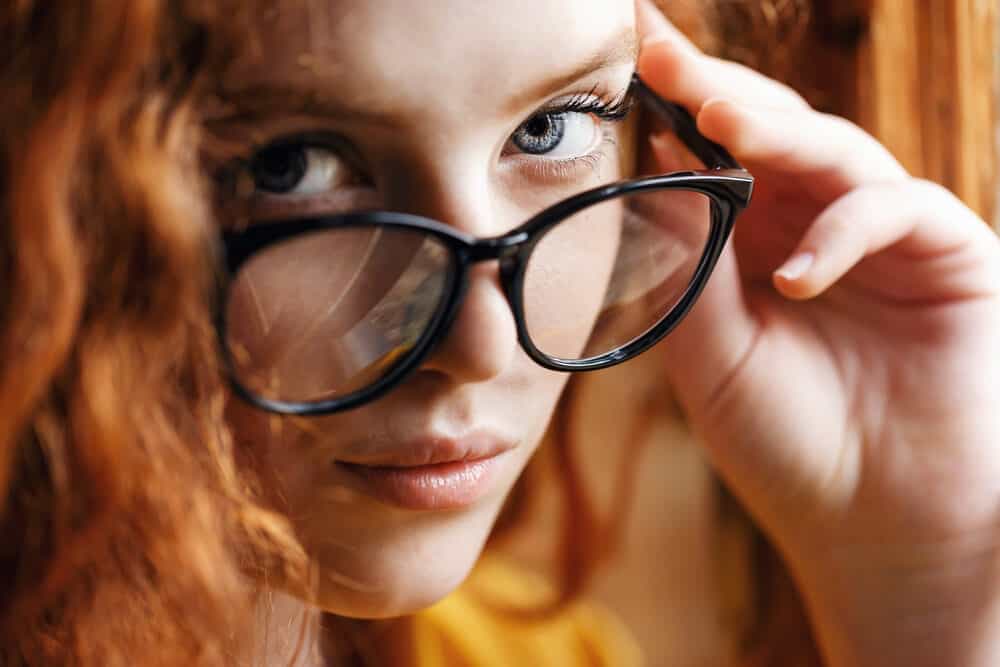 Close-up of a cute white girl wearing reddish permed hair with dark-colored glasses.