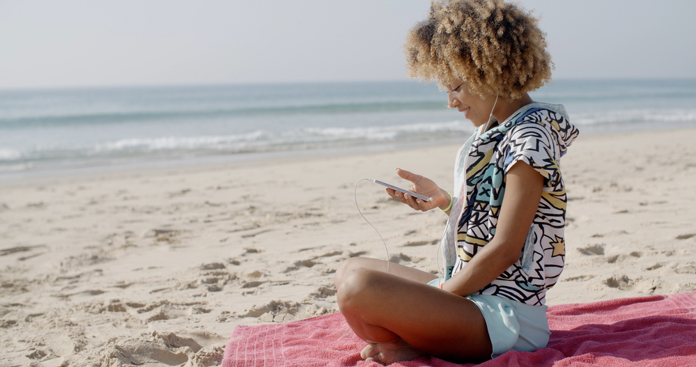 Lady sitting on a beach towel near the beach reading about hair cuticle damage from hair bleach.