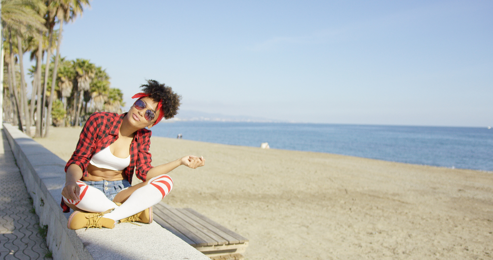 Fashionable young woman with healthy hair with a 4A natural curl pattern sitting near the sea.