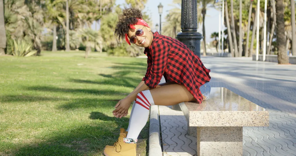 Stylish young black female with dry hair in a curly updo wearing a red and black plaid shirt with jean shorts.