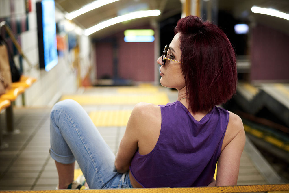 Young woman wearing a dark purple shirt with blue jeans while waiting for the subway.