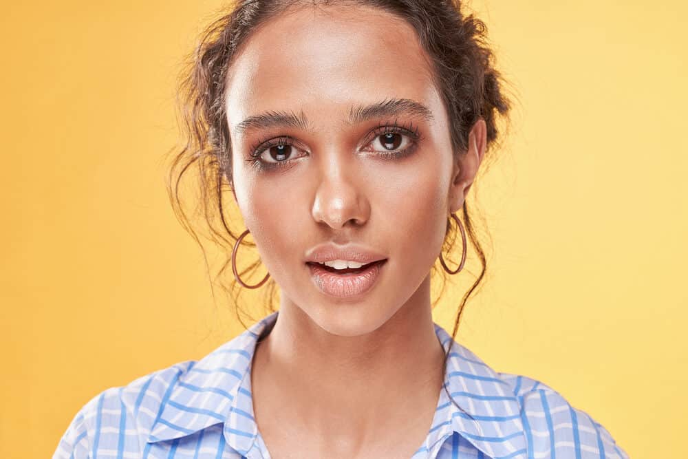 Young black girl with brown frizzy curls wearing a blue plaid shirt dress and hoop earrings